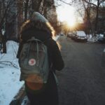 Woman in black jacket and brown backpack standing on road during daytime
